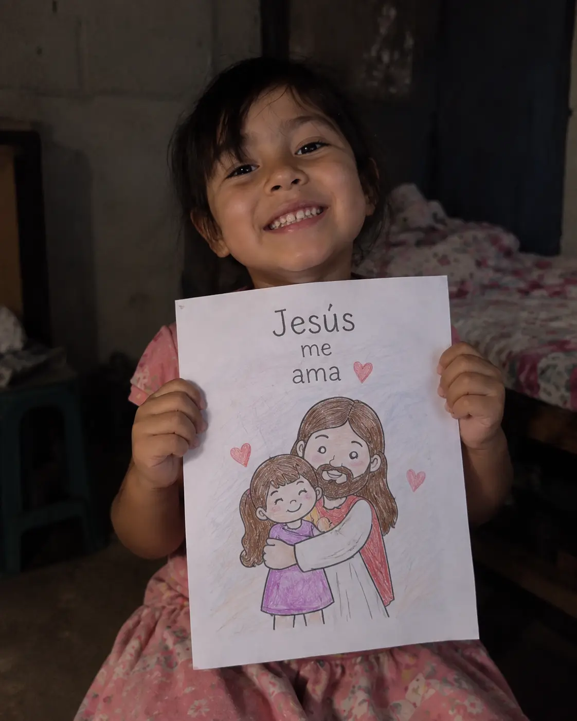 Niña sonriente mostrando una actividad coloreada con el texto Jesús me ama
